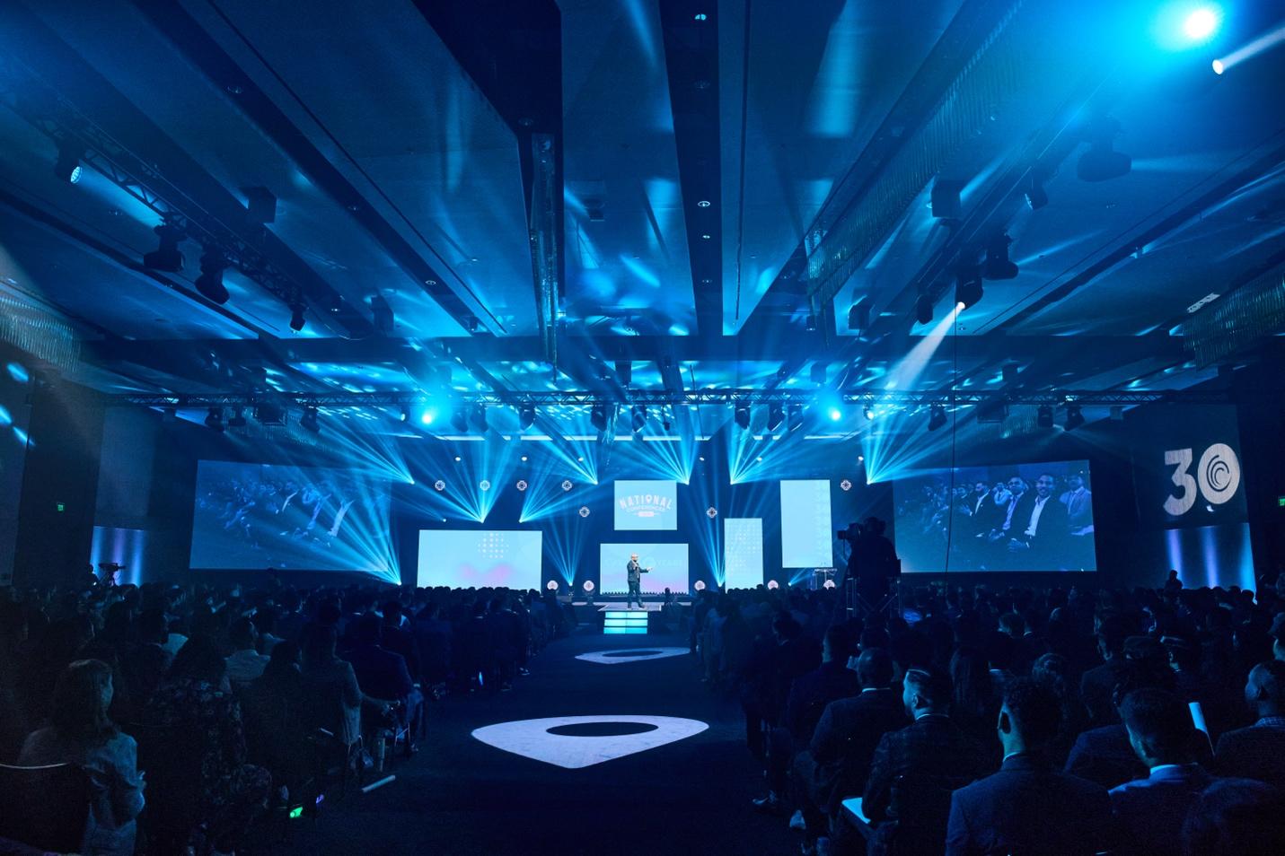 A group of people sitting in a room with a stage with blue lights